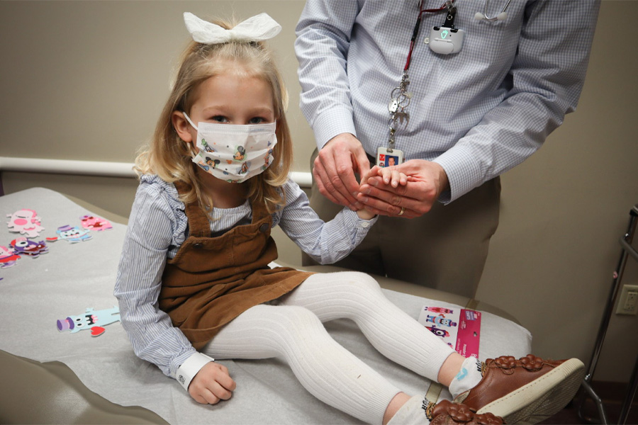 A girl wearing a mask sits on an examination table