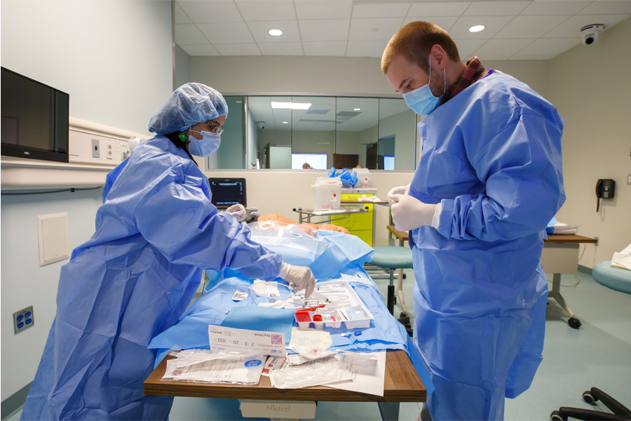 Two students wearing personal protective equipment participate in a simulated medical procedure