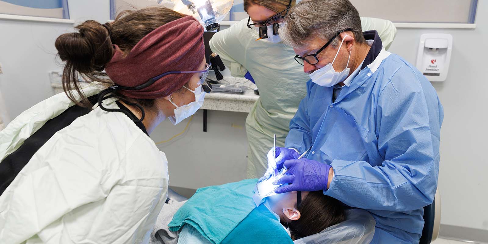 A patient receives dental care from a dentist/faculty member and two students.