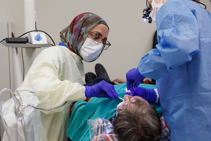 A female student wearing a headscarf works with a faculty member to provide patient care.