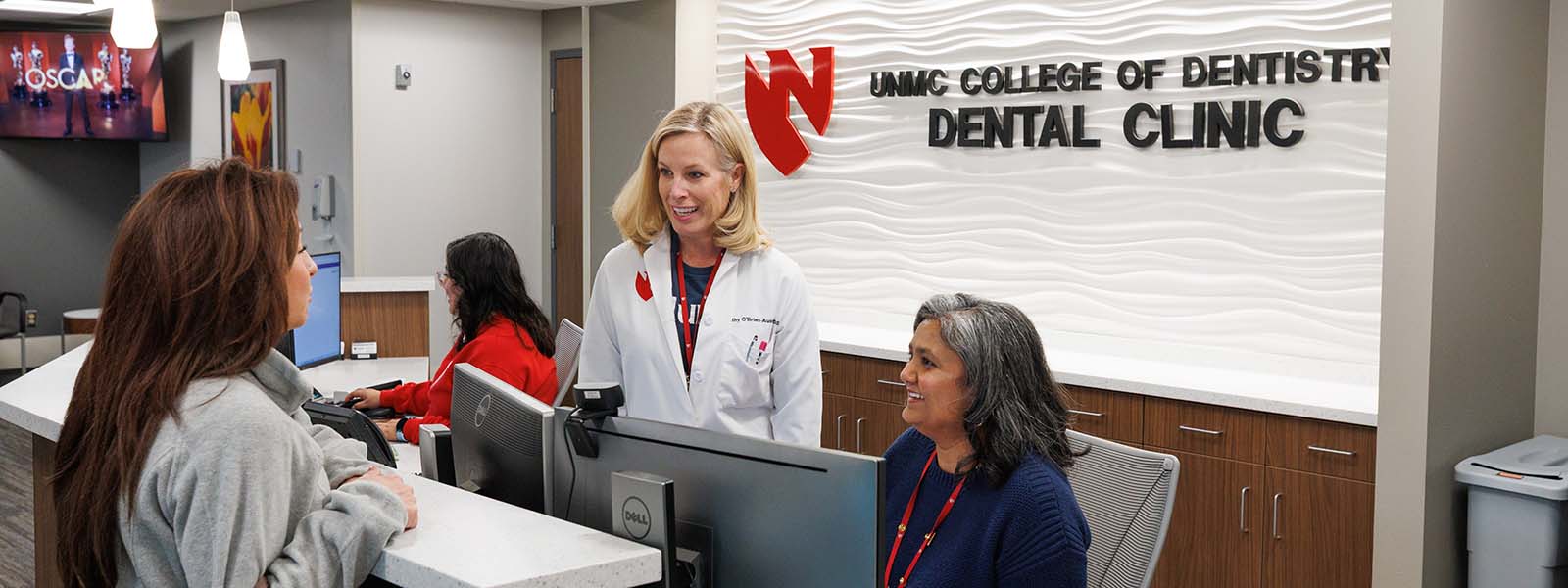 A dentist and a staff member confer at the front desk of the Omaha clinic.
