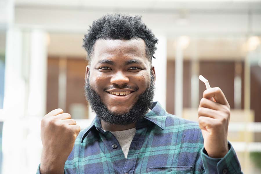 Smiling African American man pumps his right fist while holding a broken cigarette in his left.