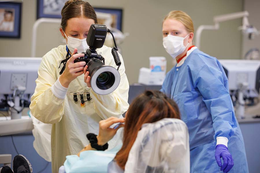 A faculty member works with a student using a camera to take dental images of a patient.