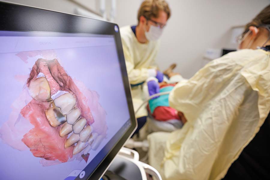 Students work in the CAD lab with a mouth model on a monitor screen.