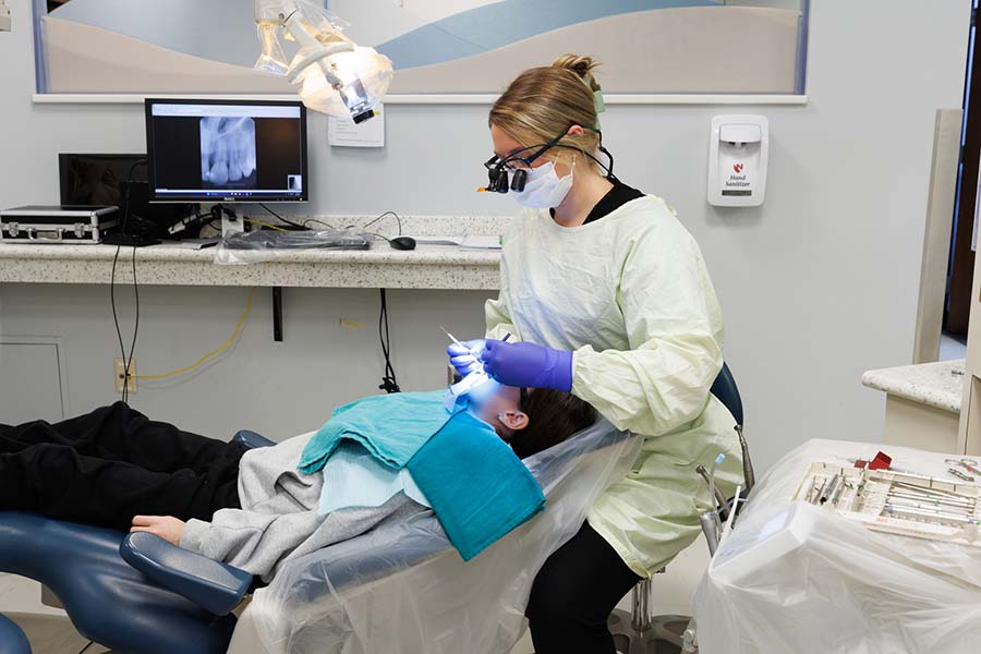 A female resident examines a patient with an x-ray on a monitor nearby.
