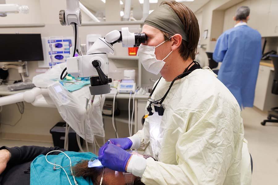 A resident uses a microscope while performing a root canal.