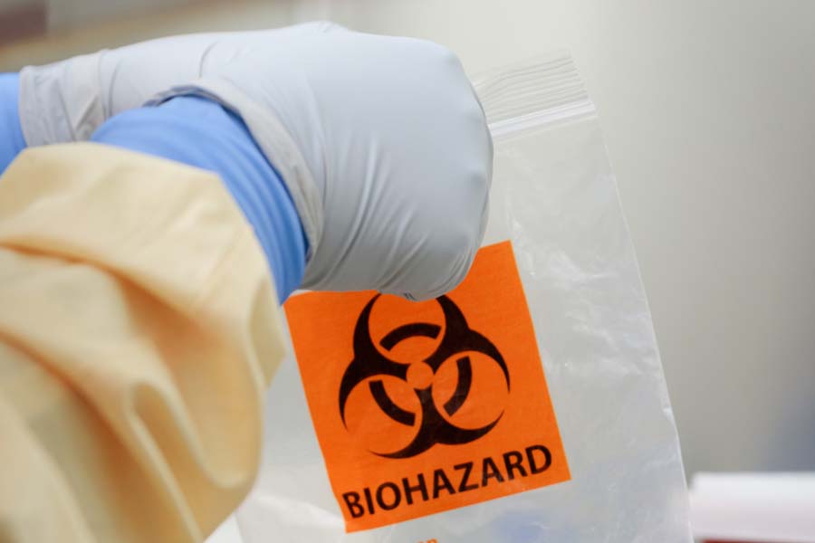 Lab worker places an item in a plastic bag marked with the biohazard label.