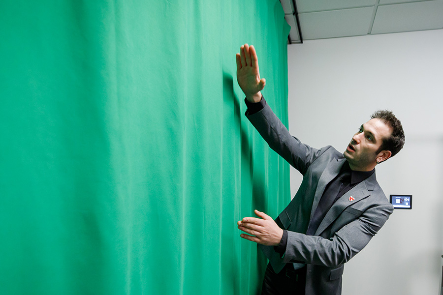 Man stands in front of green screen to demonstrate how to use the green screen mode.