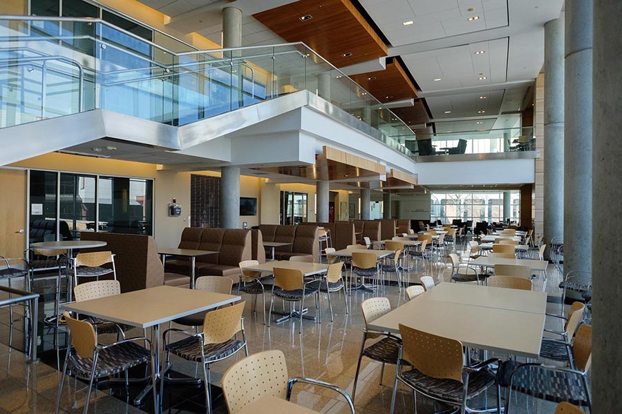 The naturally lit Alumni Commons area sits empty with tables and chairs.