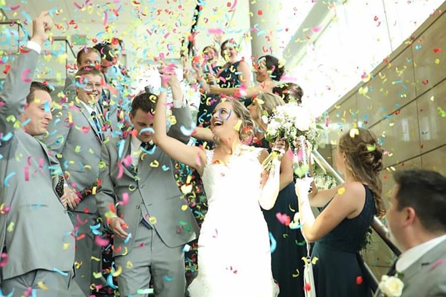 A newly married couple makes grand entrance while the wedding party shoots confetti.