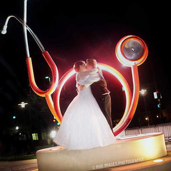 The happy couple kiss in front of the stethoscope sculpture in front of the Sorrell Center.