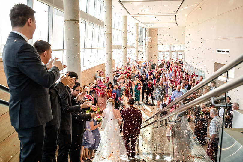 A newly married couple makes grand entrance while the wedding party shoots confetti.