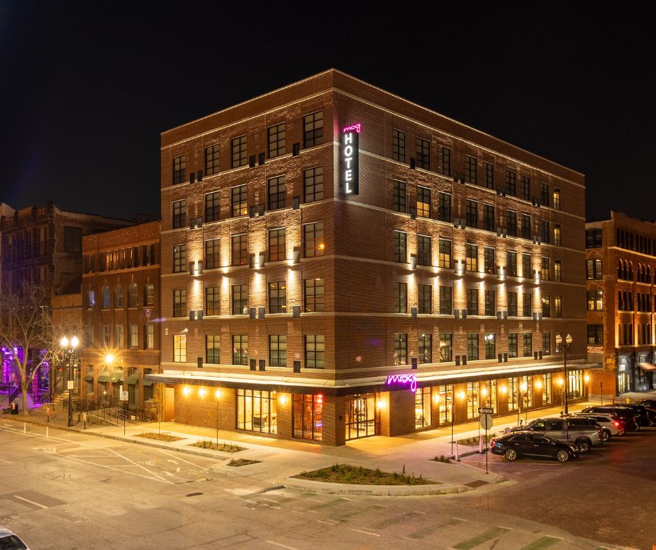 A brick building on a city corner at night, with "Moxy Hotel" on a lit sign.