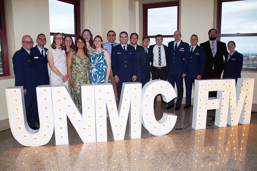 group of men and woman behind large marquee letters that say UNMC FM