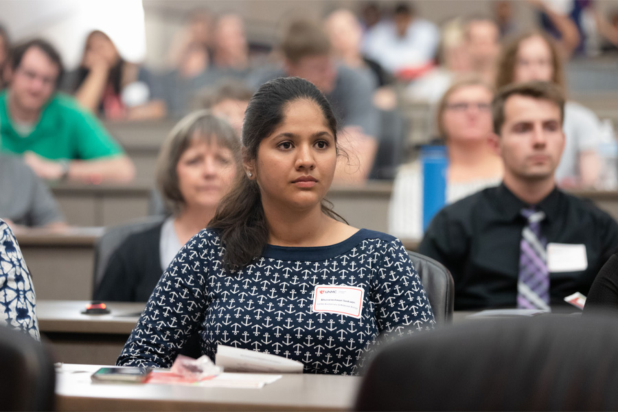 A woman wearing a name tag listens to a speaker out of frame.