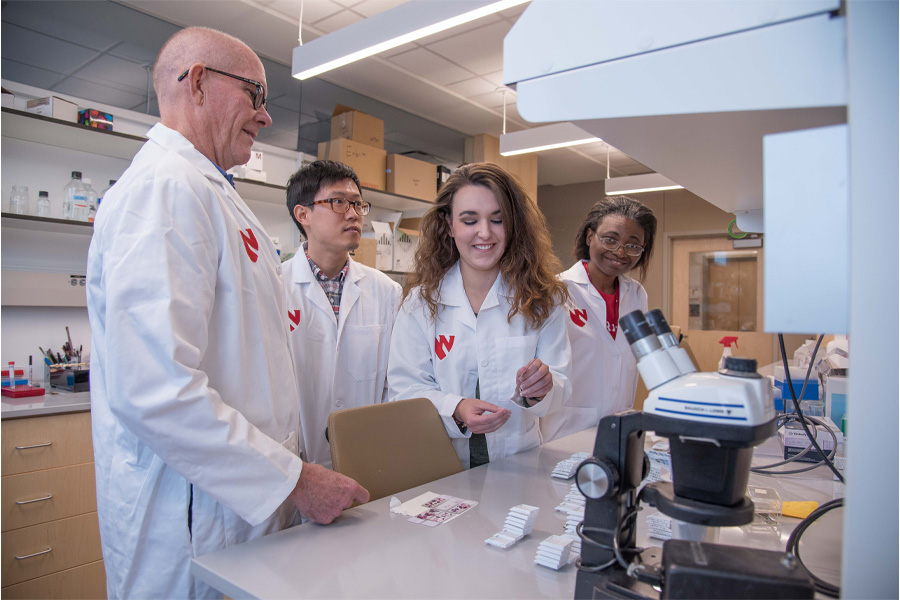 Four people in white coats work in a lab.