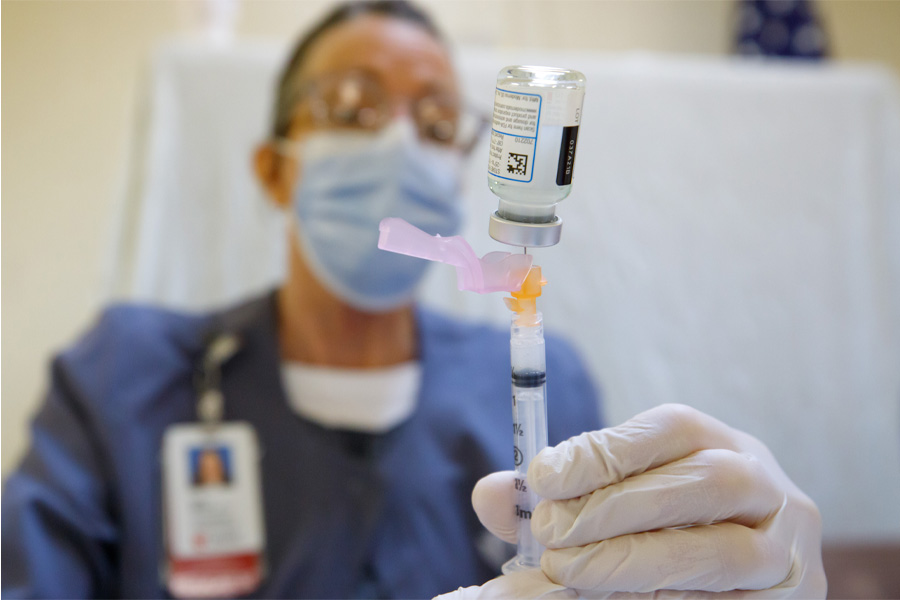 A man wearing glasses and a surgical mask injects liquid into a syringe.