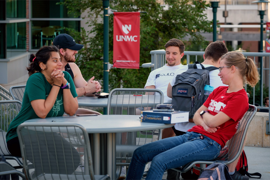 UNMC students sit around tables outside on the Omaha campus.