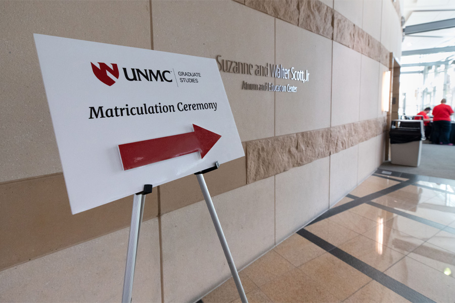 A sign in a hallway reads "Matriculation Ceremony" with an arrow pointing right