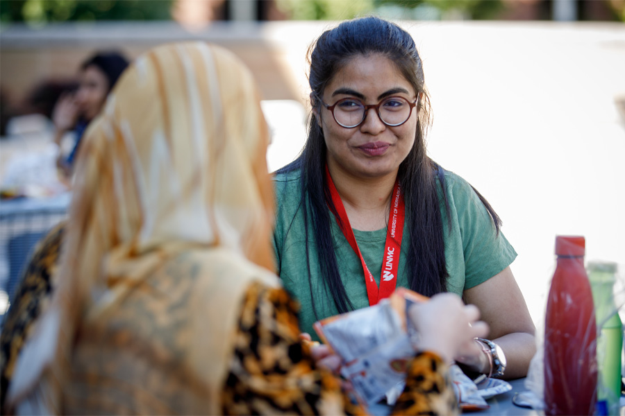 A woman wearing glasses speaks to a woman wearing a head covering.