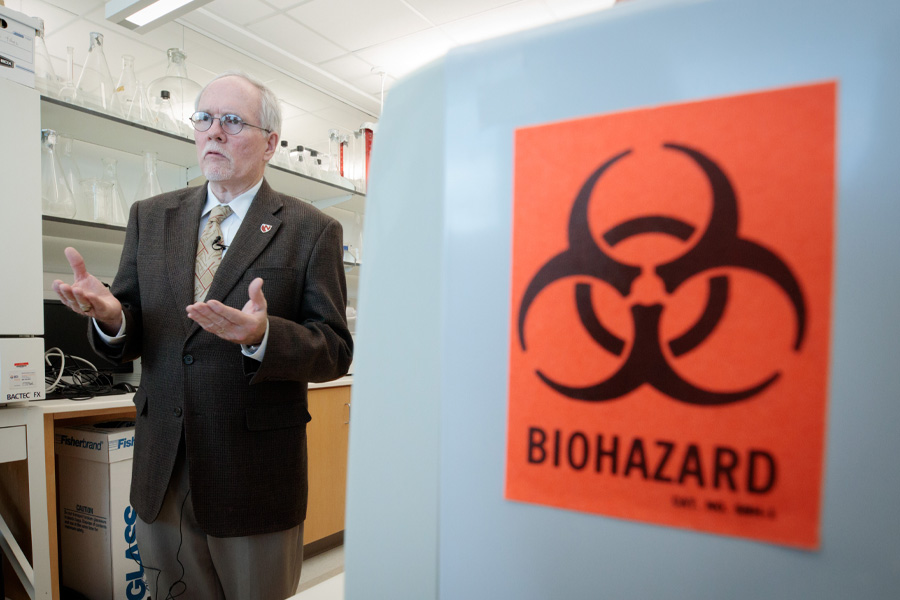 A man speaks next to a metal barrel with a sign on it reading "Biohazard."