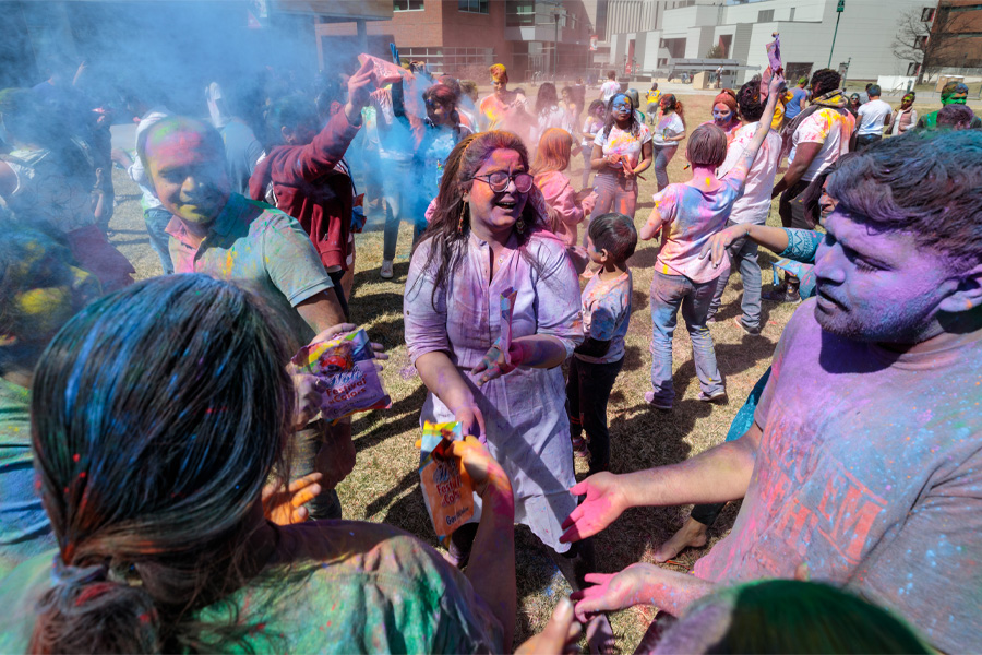A large group of people throw colored powder during a Holi celebration.