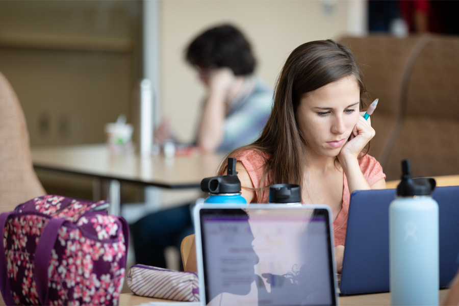 A female student rests her chin on her hand as she works on a laptop