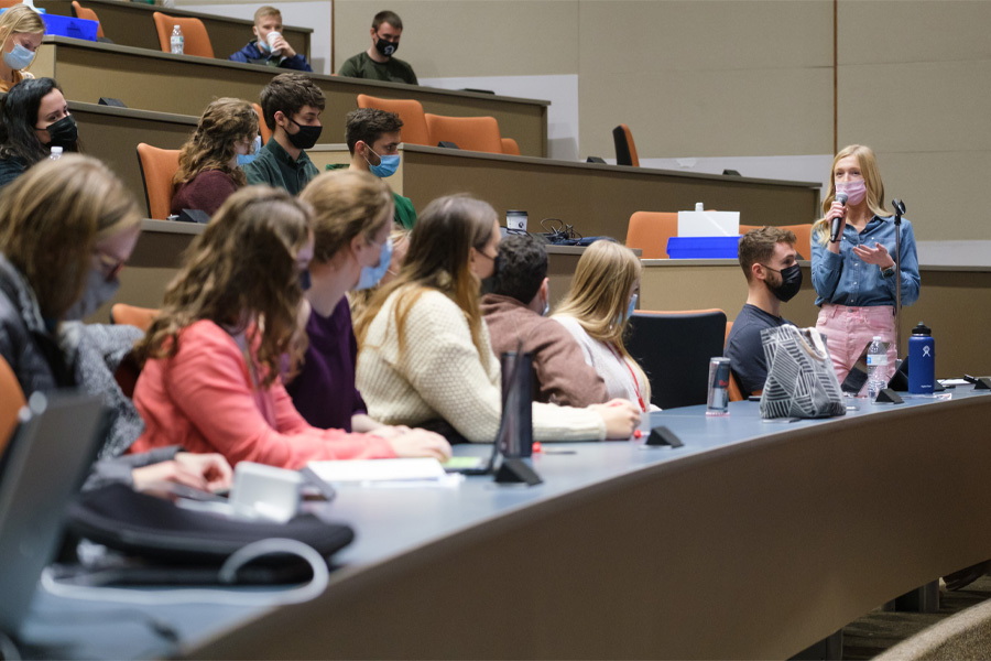 A woman holds a microphone and speaks to fellow students in a lecture hall