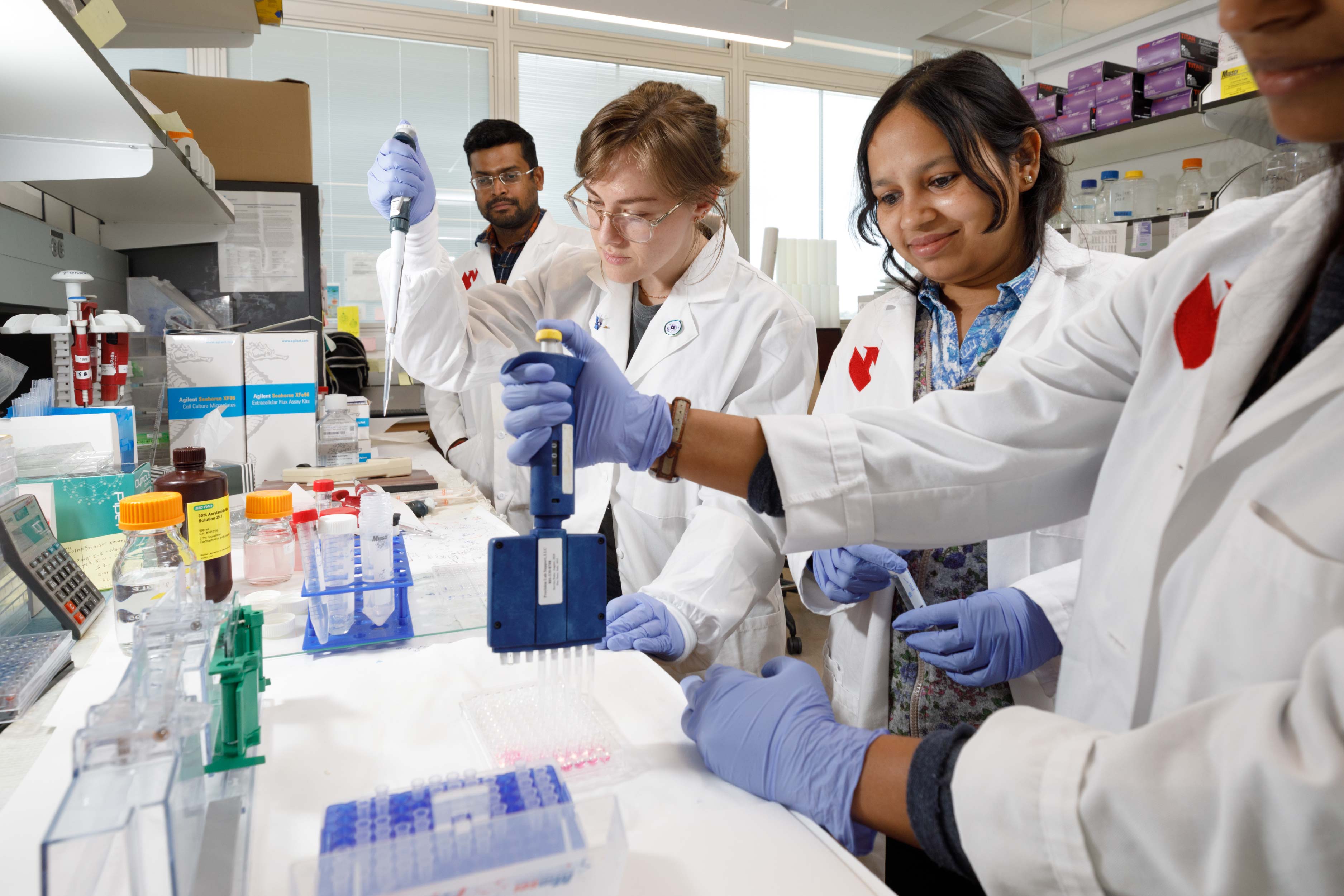 Four researchers in white lab coats work with research equipment in a lab