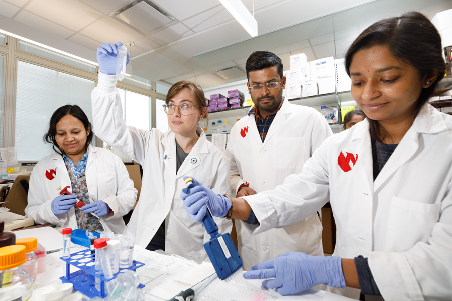 A group of four researchers wearing white lab coats work in a lab