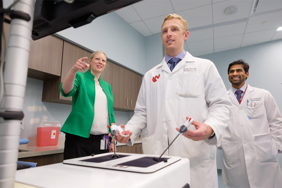 A professor watches a student work with medical equipment