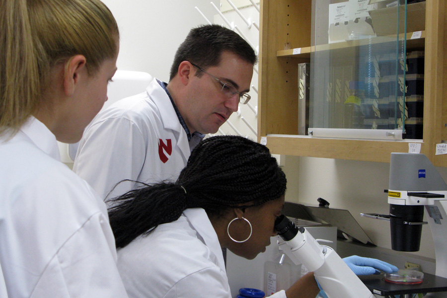 Three researchers in white coats work on a lab