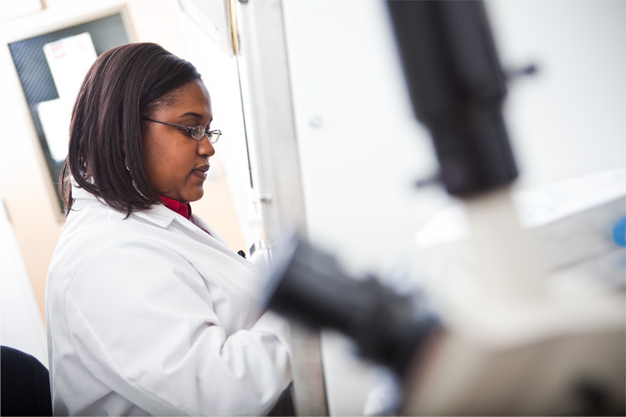 A woman in a white lab coat works with a microscope