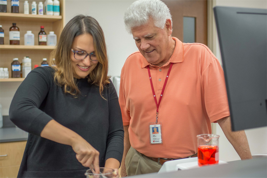 A man observes a woman working with research equipment.