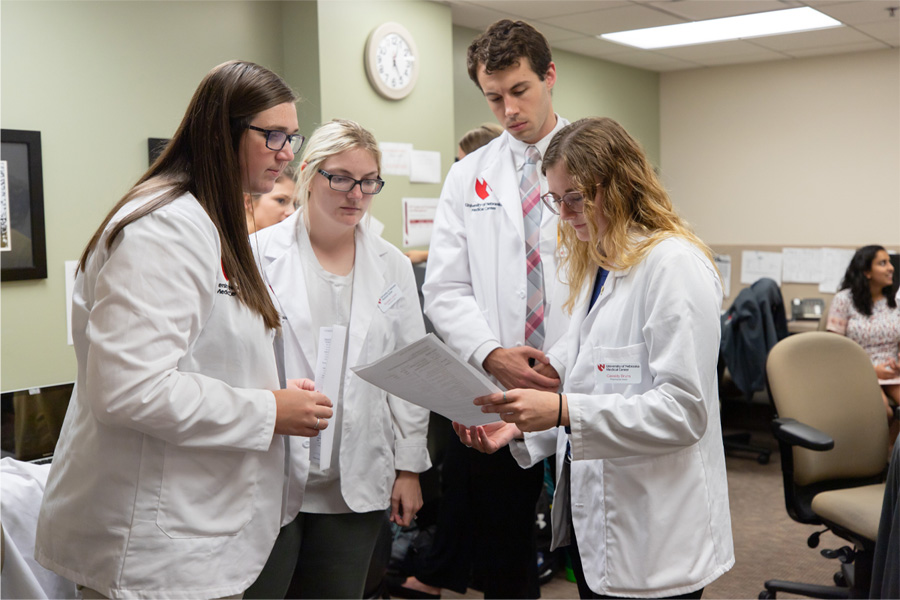 A group of people in white lab coats consult over paperwork