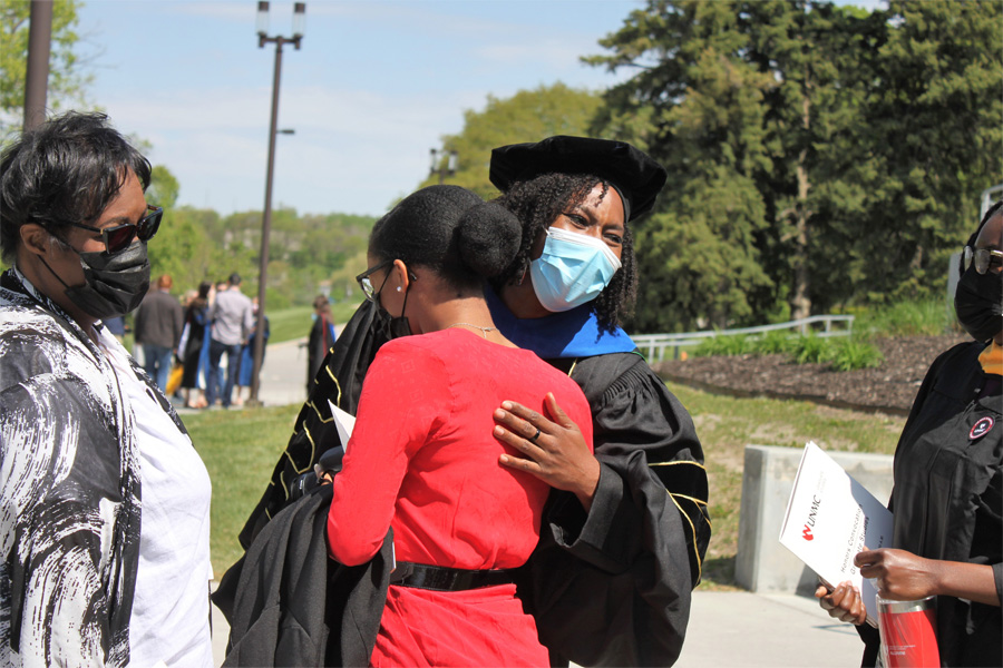 A woman wearing academic regalia is hugged by another woman.