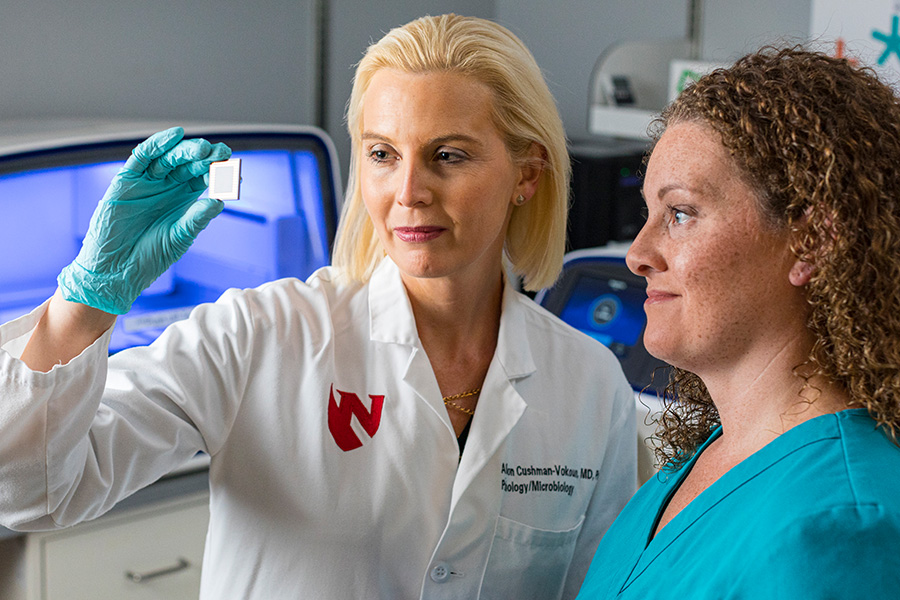 Faculty member holds up a microscope slide and discusses it with a student