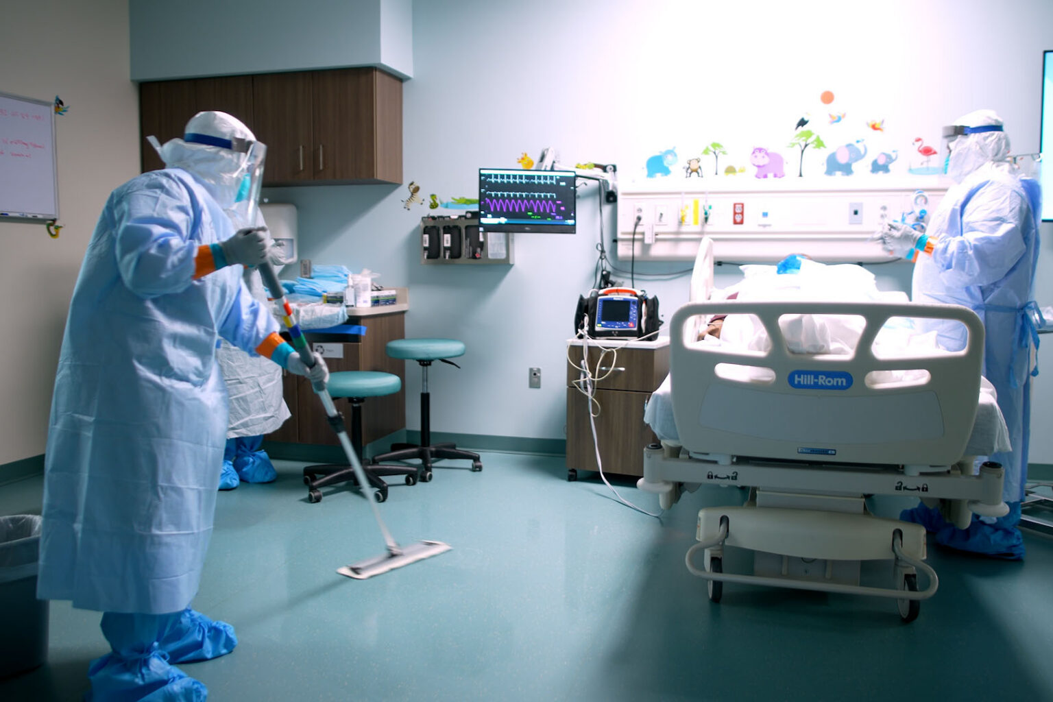 A medical professional from the Center for Sustainment of Trauma and Readiness Skills (C-STARS) Omaha, in full personal protective equipment, mops the floor while another team member tends to a simulated patient at the University of Nebraska Medical Center.