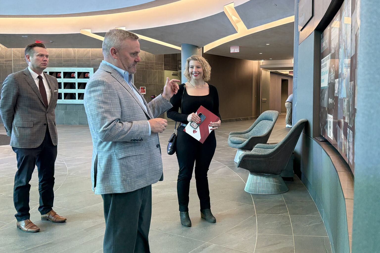 Three people tour the UNMC Davis Global Center, viewing a large interactive display during a visit highlighted