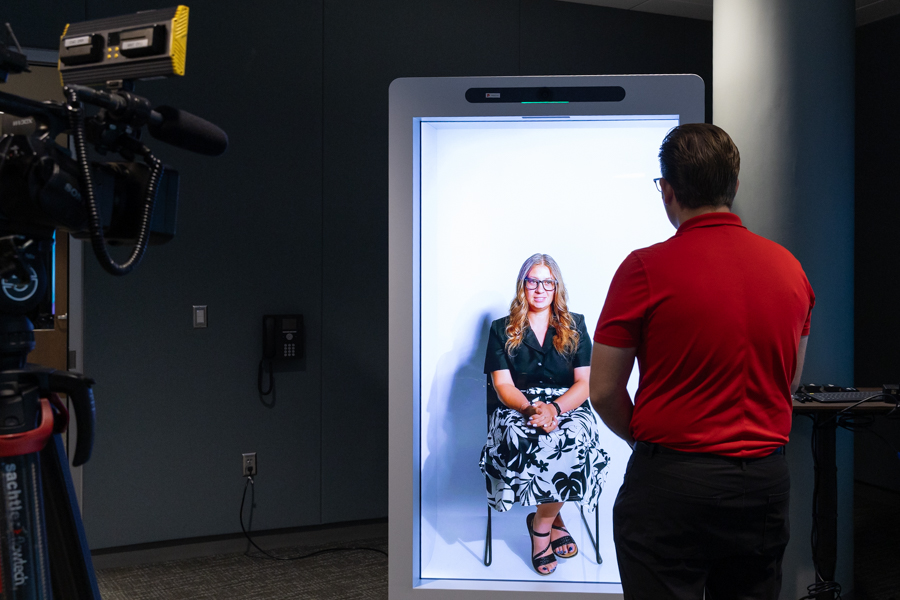 Cheyanne Wood sits in a holographic box while being interviewed by a reporter