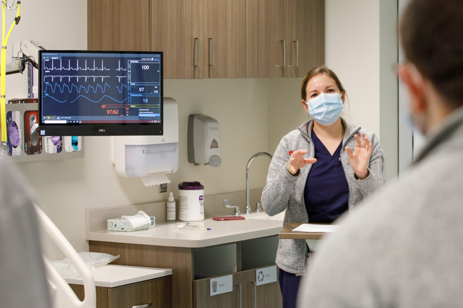 A female physician speaks to students in a patient's room