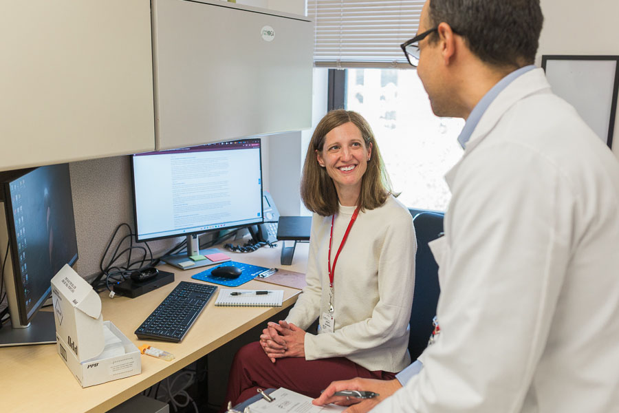 Two people sit in an office space, smiling at one another.