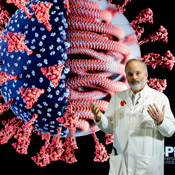 Dr. James Lawler stands in front of a display of the COVID-19 virus