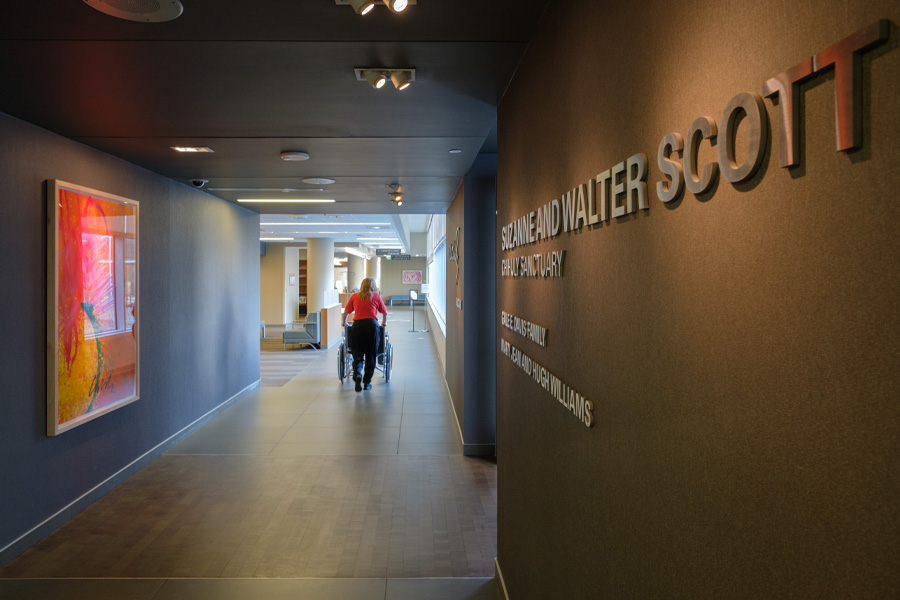 A woman pushes someone in a wheelchair down a hallway
