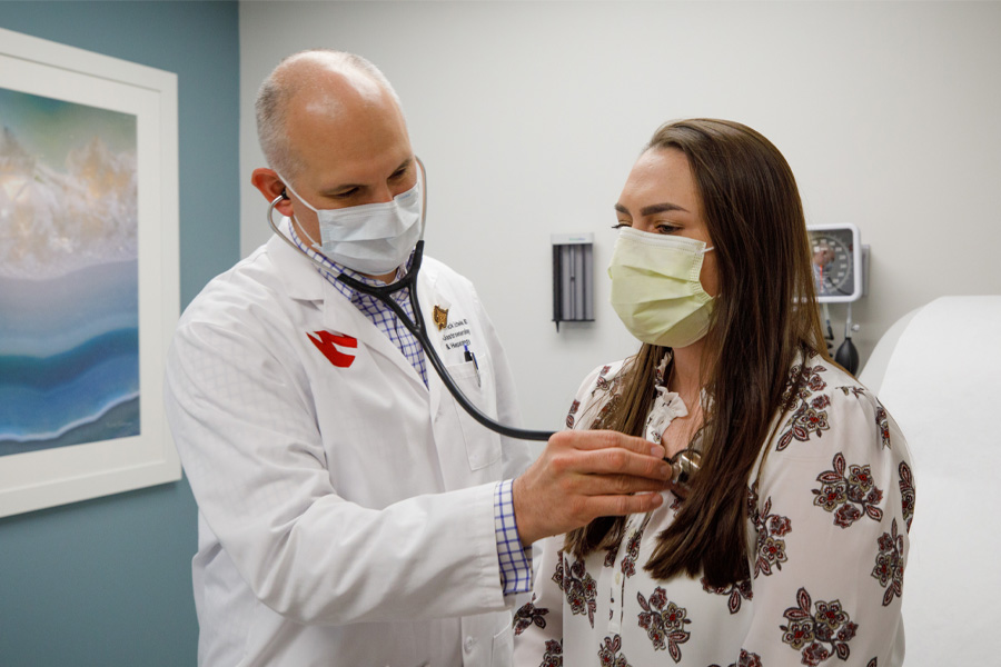 A male doctor uses a stethoscope to listen to a female patient's lungs