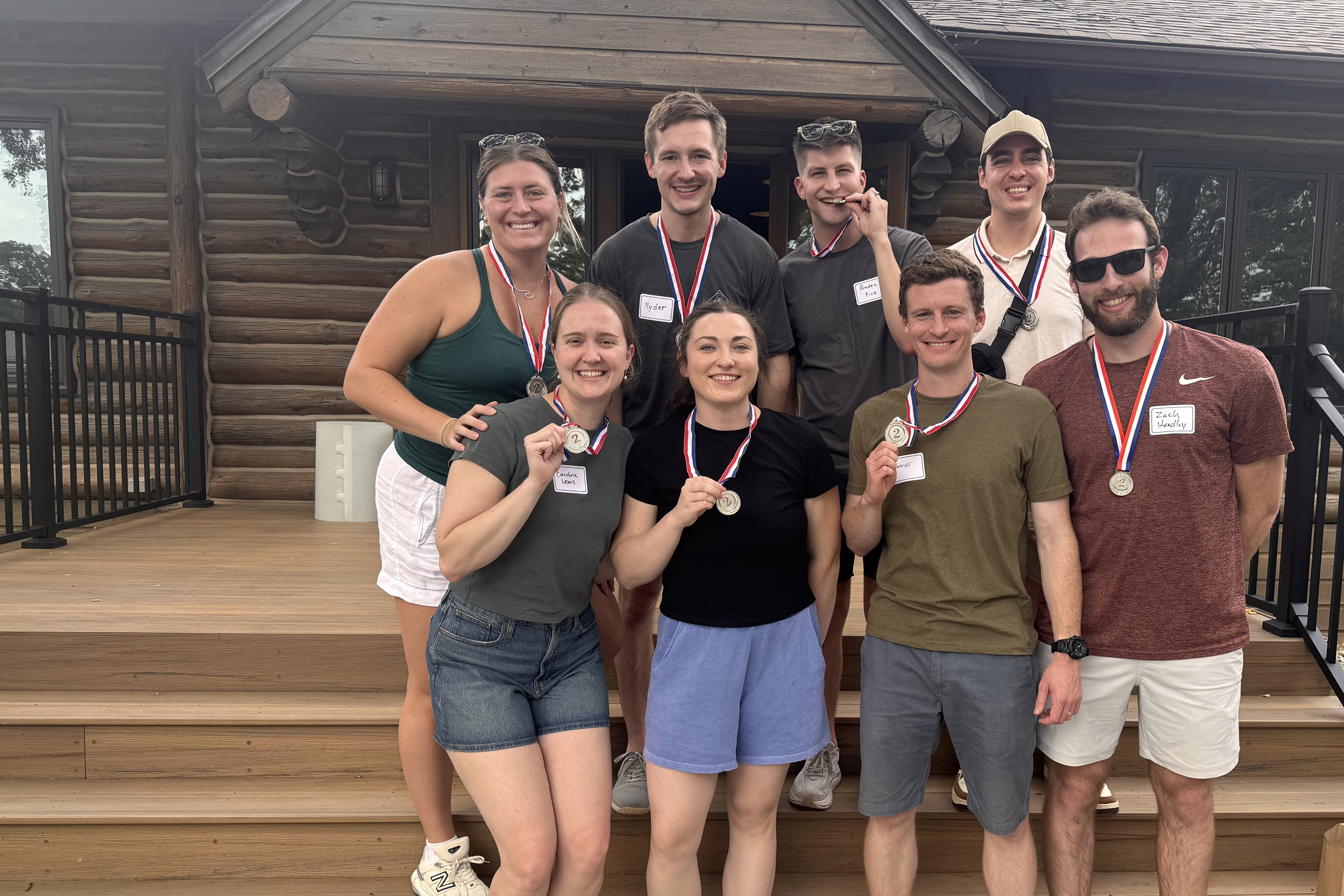 A group of eight residents pose outdoors in front of a cabin wearing medals around their necks after a resident wellness event.