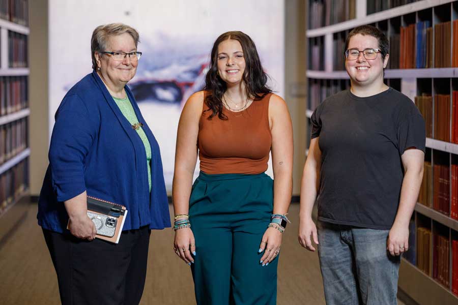 Three people standing in hallway of bound journals.