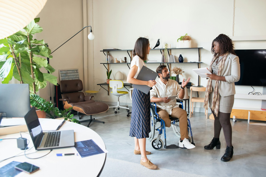 Three adults have a meeting, the individual in the center sits in a wheelchair.