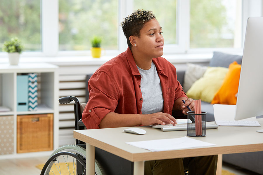 Adult in wheelchair working on a computer in a sunny office.
