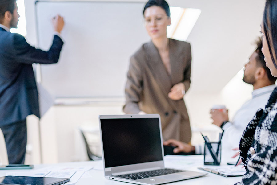 Two people standing presenting to people sitting with laptop at table, credit Yan Krukau – Pexels. 